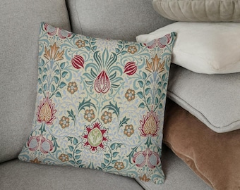 May include: A decorative square pillow with a floral pattern in shades of red, blue, green, and gold. The pillow is placed on a gray sofa, with other pillows in various colors and textures in the background.