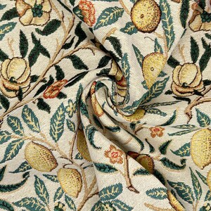 May include: Close-up of a cream-colored fabric with a repeating pattern of green leaves, yellow lemons, and orange flowers. The fabric is woven with a textured surface.