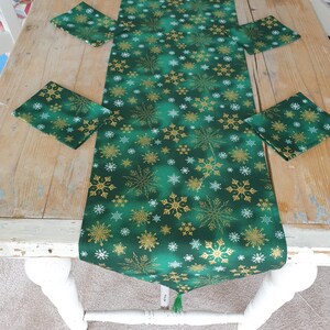 May include: A green table runner with a gold snowflake pattern. The runner is on a wooden table with four matching placemats.