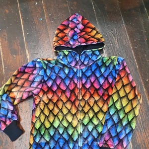 Op de afbeelding: Een regenboog draak schubben print hooded jas met een zwarte rits. De jas is gemaakt van een zachte, pluche stof.