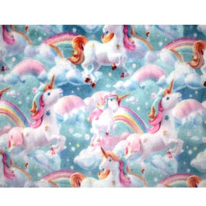Può includere: Un design di tessuto stravagante con unicorni bianchi con criniere e code rosa e arancioni, su uno sfondo di arcobaleni pastello, nuvole soffici e un cielo azzurro. Gli unicorni hanno corna dorate e dettagli a stella.