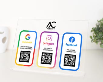 Op de afbeelding: Een helder acryl bord met drie kaarten. De kaarten hebben QR-codes en social media logo's voor Google, Instagram en Facebook. De tekst op de kaarten luidt "Laat ons een recensie achter op Google", "Volg ons op Instagram" en "Volg ons op Facebook".