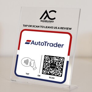 May include: A white sign with red and blue trim, featuring the AutoTrader logo and a QR code. The sign reads "Tap or Scan to Leave Us a Review".