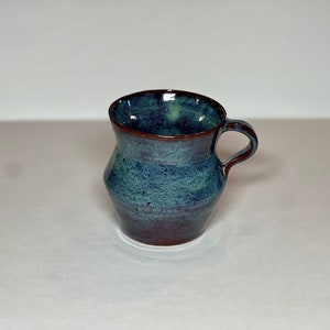 May include: A small, blue and brown ceramic mug with a rounded body and a handle.