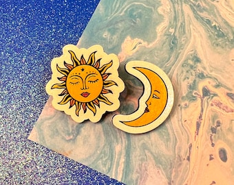 May include: Two wooden cutouts, one of a yellow sun with a face and the other of a yellow crescent moon with a face. Both have a whimsical, retro style.