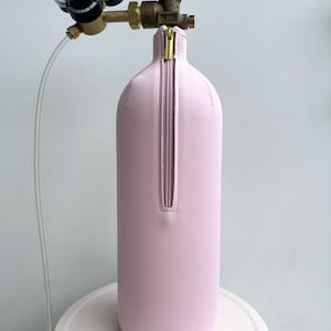 May include: A pink, cylindrical tank with a zippered cover and a brass valve on top. The tank is connected to a regulator with two gauges.