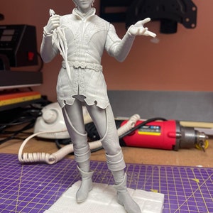 Può includere: Statuetta in resina non verniciata di un uomo in abiti d'epoca, con una spada. La figura è su una base strutturata, con dettagli intricati sui vestiti e sul viso. La statuetta è alta circa 25 cm.