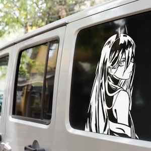 May include: A white vinyl decal of an anime-style character is affixed to the rear window of a silver vehicle. The character has long hair and is facing to the side. The background is black.
