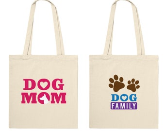 May include: Two beige canvas tote bags with different designs. The first bag has the text "DOG MOM" in pink with a white dog silhouette inside a pink heart. The second bag has two brown paw prints and the text "DOG FAMILY" in blue with a pink heart.