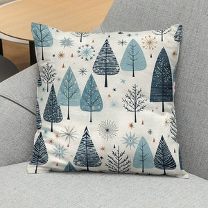 Könnte beinhalten: Quadratisches Kissen mit einem Winterwaldmuster. Das Kissen zeigt stilisierte blaue Bäume, Schneeflocken und Sterne auf cremefarbenem Hintergrund. Die Bäume haben verschiedene Texturen und Blautöne. Das Kissen liegt auf einem grauen Sessel.