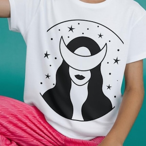 May include: White t-shirt with a black and white illustration of a woman with a crescent moon over her head and stars in the background.