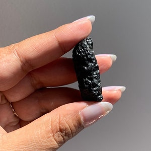 May include: A dark gray, rough-textured, irregularly shaped rock, held in a hand.