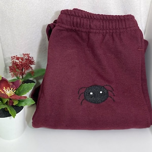 May include: Burgundy sweatpants with a black embroidered spider with white eyes.