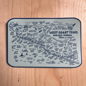 Peut inclure: Une carte rectangulaire bleu clair du West Coast Trail sur l'île de Vancouver, au Canada. La carte détaille les points de repère, les distances et le texte "75km-ish (feels like more)". La carte comprend des illustrations de baleines, d'aigles et d'autres animaux sauvages.
