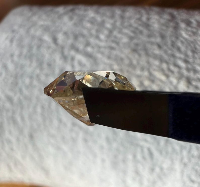 May include: A clear, faceted, light brown gemstone held in a black metal tweezer.