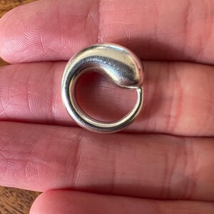 May include: A silver-coloured, curved earring with a rounded top and a circular bottom. The earring is smooth and shiny, reflecting light. The jewellery is a simple, elegant design.