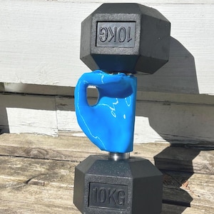 Può includere: Due manubri neri da 10 kg impilati uno sopra l'altro. Il manubrio superiore poggia su un'impugnatura in plastica blu.