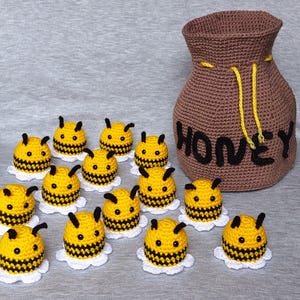 Puede incluir: Una bolsa de crochet marrón con la palabra "Honey" en ella, rodeada de 14 abejorros de crochet con rayas negras y amarillas.