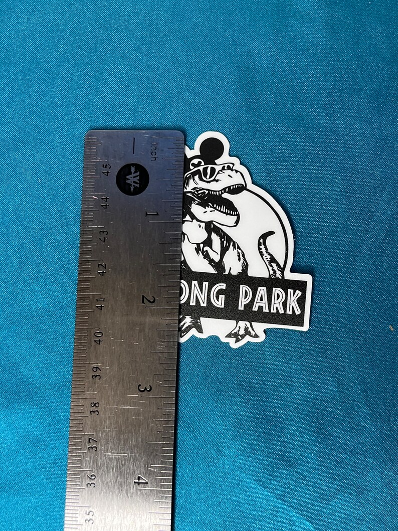 May include: A black and white sticker featuring a dinosaur wearing sunglasses and a Mickey Mouse-style head. The sticker reads "ONG PARK" in a stylized font. The sticker measures approximately 4 inches in height.
