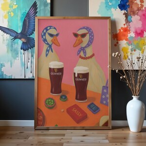 K&ouml;nnte beinhalten: Gerahmtes Gem&auml;lde mit zwei anthropomorphen G&auml;nsen mit Sonnenbrille und Kopftuch, mit zwei Pints Guinness. Das Gem&auml;lde hat einen rosa Hintergrund und einen Tisch mit einer roten Box mit der Aufschrift "SASSY". Weitere Gegenst&auml;nde auf dem Tisch sind ein Telefon und ein kleines Spielzeug.