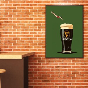May include: A framed art print featuring a pint of Guinness stout with a diver in a red swimsuit. The Guinness logo is visible on the glass. The background is green, and the print is displayed on a brick wall.