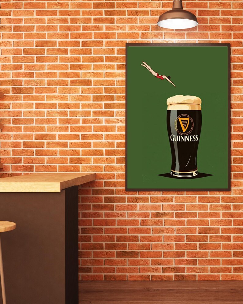 May include: A framed art print featuring a pint of Guinness stout with a diver in a red swimsuit. The Guinness logo is visible on the glass. The background is green, and the print is displayed on a brick wall.