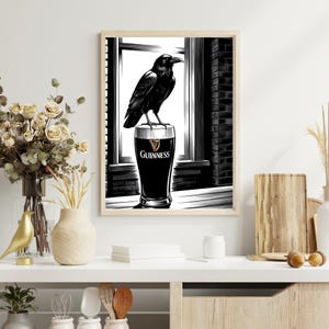 May include: Black and white illustration of a raven perched on top of a glass of Guinness beer. The raven is looking to the right. The glass is on a table in front of a window.