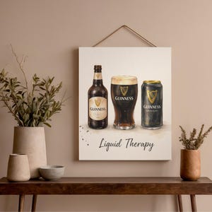 May include: A canvas print showing a watercolour illustration of Guinness stout. The artwork depicts a bottle, a pint, and a can of Guinness. The words "Liquid Therapy" are written below the images. The print is hanging on a wall.