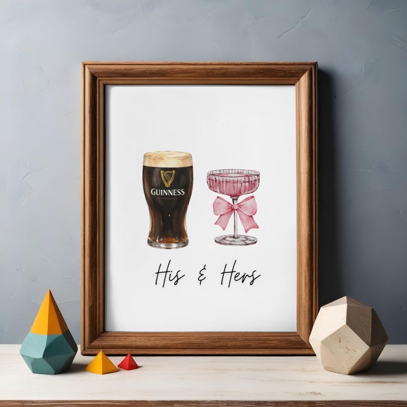 Puede incluir: Impresi&oacute;n enmarcada con ilustraciones de acuarela de una pinta de Guinness y una copa de champ&aacute;n rosa con un lazo. El texto "His & Hers" est&aacute; escrito debajo. El marco es de madera marr&oacute;n.