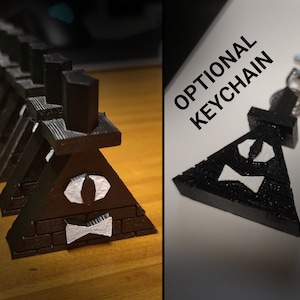 May include: A black 3D printed pyramid with a white eye and bow tie design. The pyramid is a popular character from the show Gravity Falls. The image also shows a keychain version of the pyramid with a silver chain.