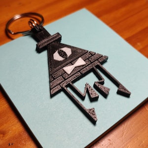 May include: Black 3D printed keychain featuring a triangle with a white eye and bowtie, and the text "BILL" written in a stylized font.