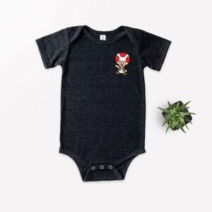May include: A dark grey baby onesie with a cartoon image of a mushroom character with a red cap and brown body.