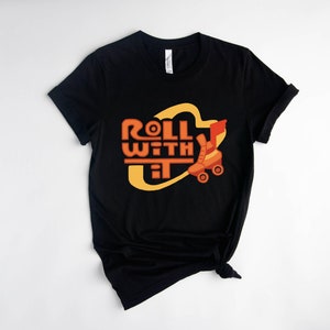 May include: Black t-shirt with a yellow and orange graphic that says "Roll With It" and features a roller skate.