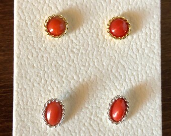 May include: A pair of red coral earrings with gold settings. The earrings are displayed on a white card.
