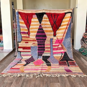 May include: A colorful Moroccan rug with geometric patterns in shades of red, orange, yellow, blue, pink, and purple. The rug has a fringe border and is woven with wool.