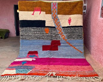 May include: A large, colorful rug with a geometric design. The rug features a brown top section, a white and black middle section, and a blue and pink bottom section. The rug has a fringe along the bottom edge.