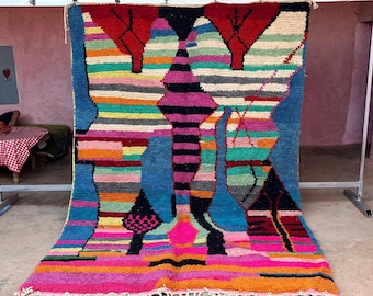 May include: A vibrant, hand-woven rug with a geometric design. The rug features a mix of bright colors, including pink, blue, red, and yellow, with a fringed edge. The design includes abstract shapes and patterns.