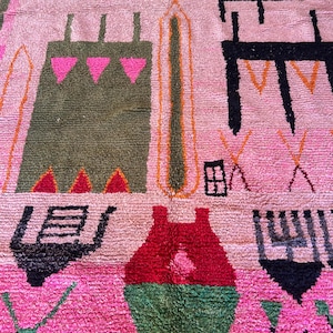 May include: A rectangular area rug featuring a soft pink background with a variety of abstract geometric shapes and symbols in black, olive green, bright pink, red, and mustard yellow. The design includes stylized motifs and linear patterns.