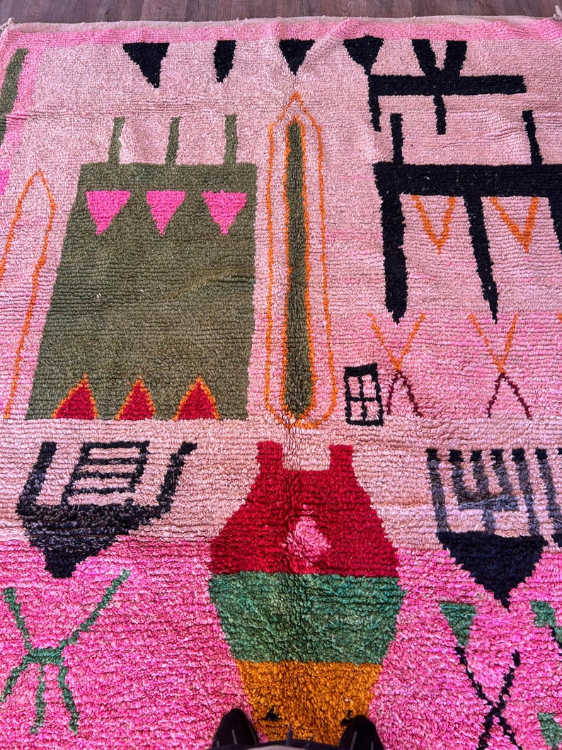 May include: A rectangular area rug featuring a soft pink background with a variety of abstract geometric shapes and symbols in black, olive green, bright pink, red, and mustard yellow. The design includes stylized motifs and linear patterns.