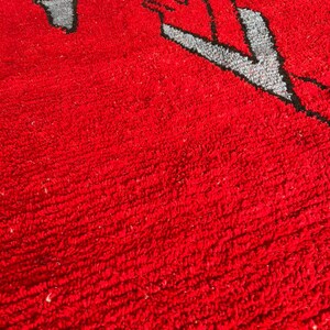 Peut inclure: Un tapis &agrave; poils longs et denses pr&eacute;sentant un fond rouge vif avec un motif graphique stylis&eacute; en gris et noir. La surface textur&eacute;e est compos&eacute;e de fibres boucl&eacute;es serr&eacute;es qui cr&eacute;ent un aspect doux et touffu sur toute la zone rectangulaire.