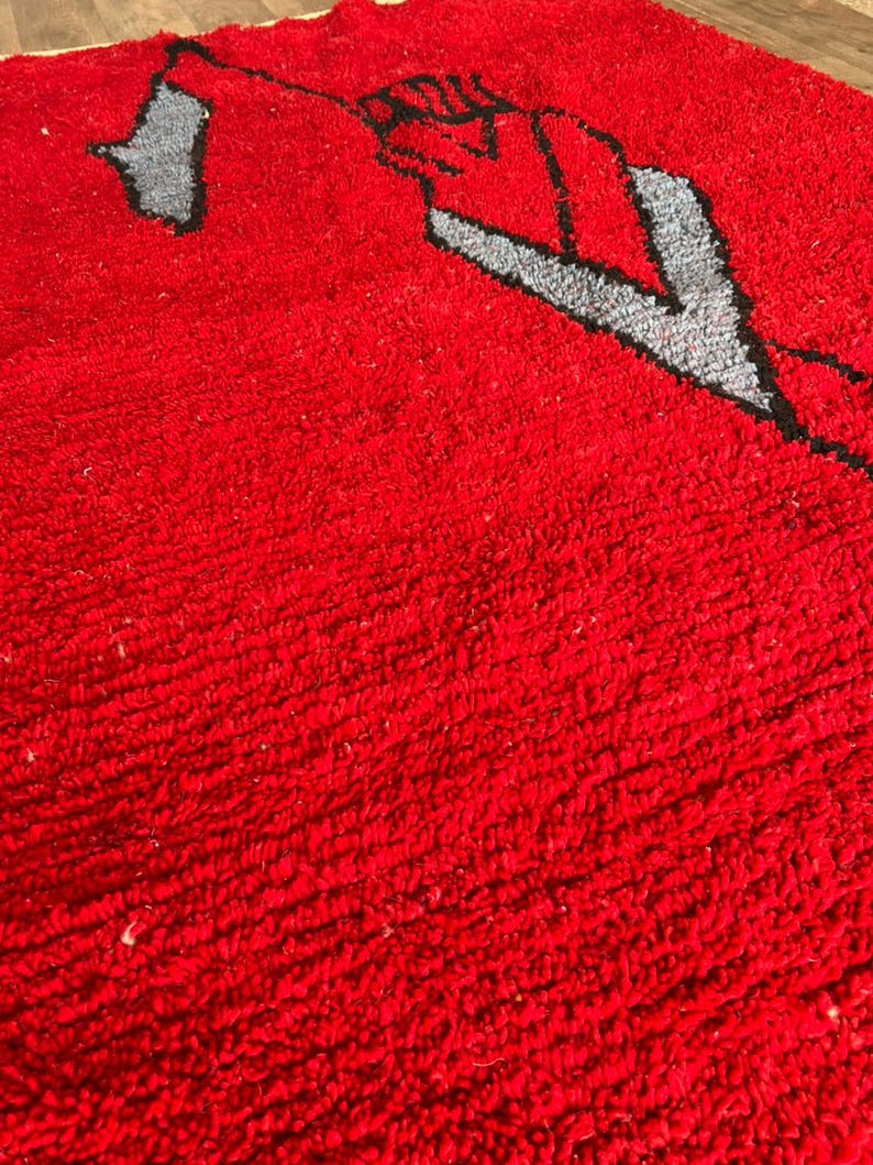 Peut inclure: Un tapis &agrave; poils longs et denses pr&eacute;sentant un fond rouge vif avec un motif graphique stylis&eacute; en gris et noir. La surface textur&eacute;e est compos&eacute;e de fibres boucl&eacute;es serr&eacute;es qui cr&eacute;ent un aspect doux et touffu sur toute la zone rectangulaire.