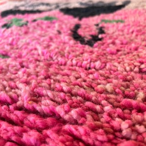 May include: A thick, high-pile rug featuring a vibrant pink base with textured, knotted wool fibers. The surface displays abstract patterns in black and muted green, creating a tactile, shaggy appearance with a deep, dense, and soft pile construction.