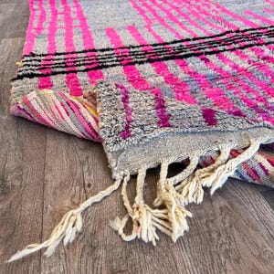 May include: A grey and pink rug with a geometric design. The rug features vertical and horizontal stripes in bright pink and black. The rug has a fringed edge.