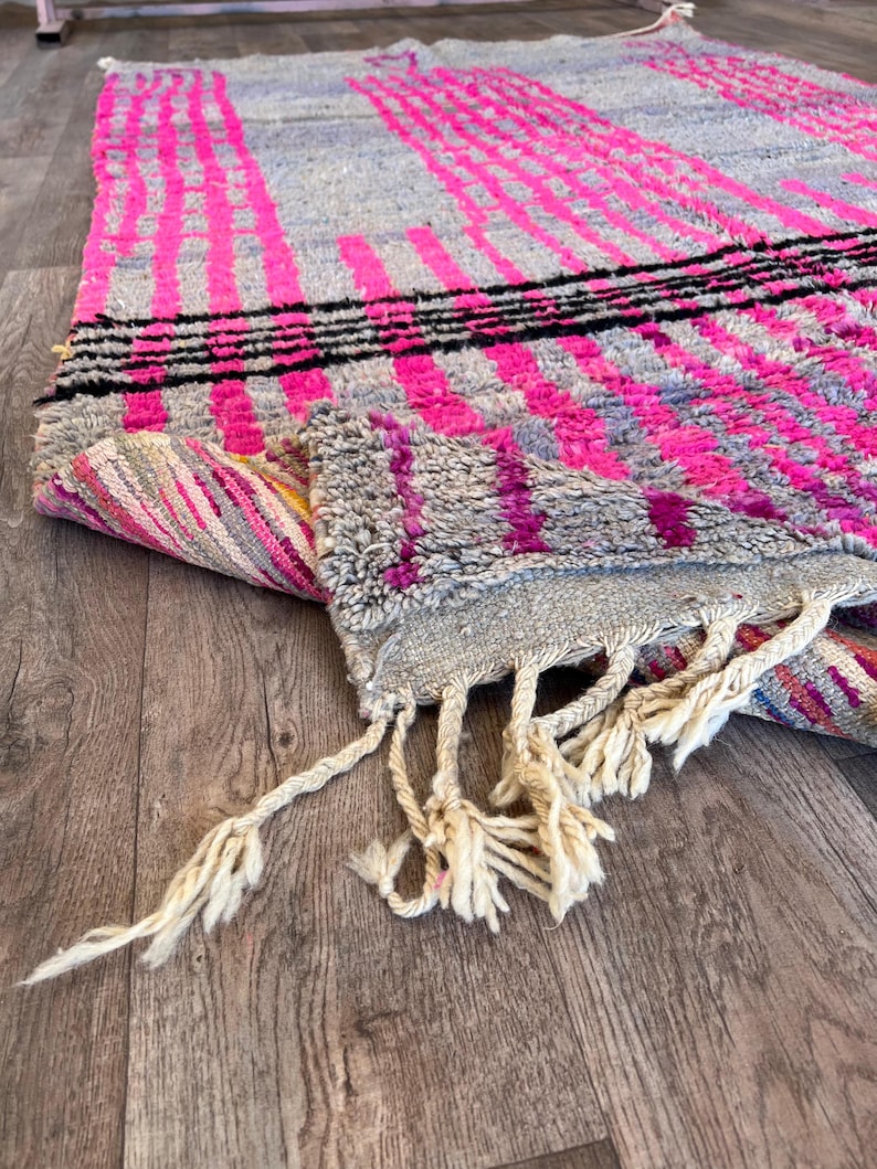 May include: A grey and pink rug with a geometric design. The rug features vertical and horizontal stripes in bright pink and black. The rug has a fringed edge.