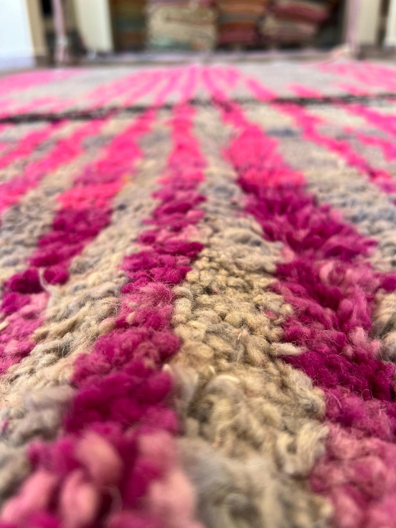 May include: Close-up of a textured rug with a pattern of vertical stripes. The stripes alternate between vibrant pink and neutral beige, creating a bold contrast. The rug's thick pile suggests a soft, comfortable texture, ideal for home decor.
