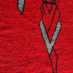Peut inclure: Un tapis rectangulaire &agrave; poils longs d'un rouge profond. Le tapis pr&eacute;sente un motif graphique abstrait et stylis&eacute;, soulign&eacute; de noir, int&eacute;grant des formes grises qui ressemblent &agrave; des &eacute;l&eacute;ments allong&eacute;s et pointus sur le fond rouge.