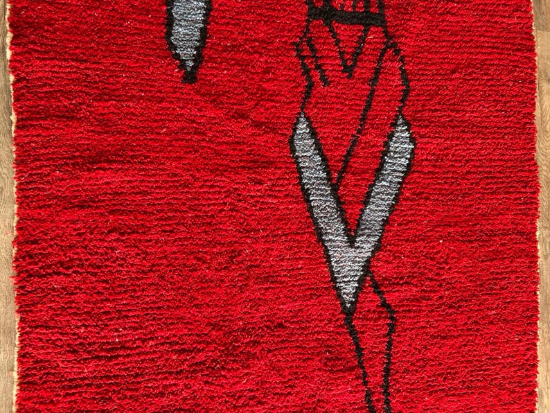 Peut inclure: Un tapis rectangulaire &agrave; poils longs d'un rouge profond. Le tapis pr&eacute;sente un motif graphique abstrait et stylis&eacute;, soulign&eacute; de noir, int&eacute;grant des formes grises qui ressemblent &agrave; des &eacute;l&eacute;ments allong&eacute;s et pointus sur le fond rouge.