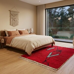 Peut inclure: Un tapis rectangulaire rouge orn&eacute; d'un motif g&eacute;om&eacute;trique noir et blanc avec des franges aux extr&eacute;mit&eacute;s. Le tapis est pos&eacute; sur un parquet en bois clair dans une chambre comprenant un cadre de lit en bois, des oreillers terracotta et une tenture.