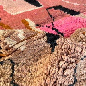 May include: Close-up of a pink, brown, and black woven rug with a textured, fuzzy surface.