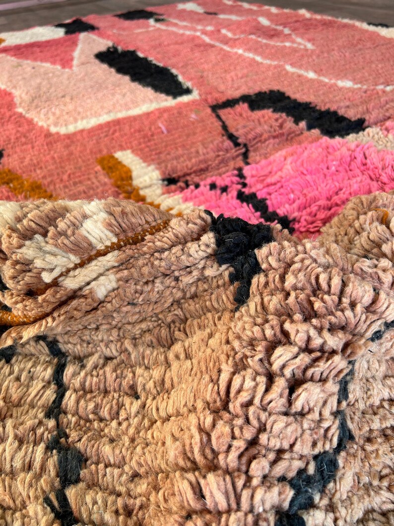 May include: Close-up of a pink, brown, and black woven rug with a textured, fuzzy surface.